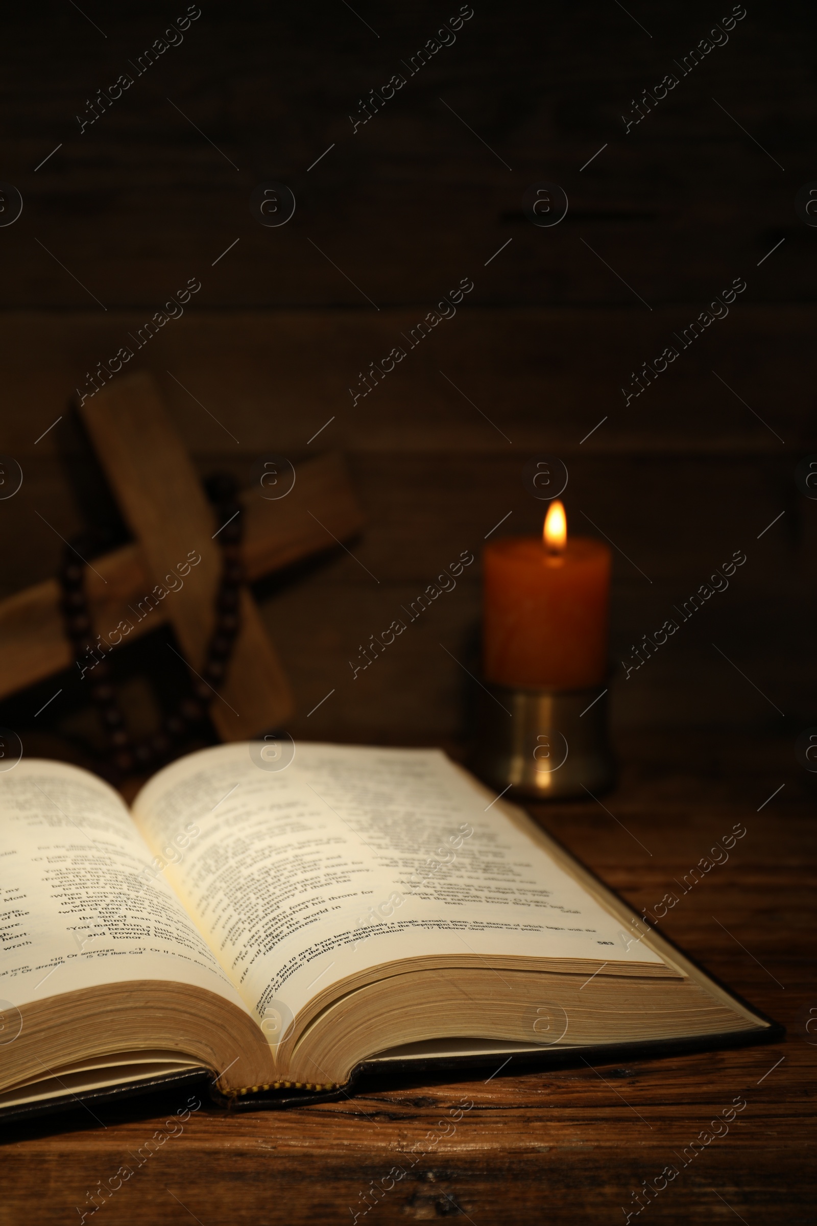 Photo of Bible, cross, rosary beads and church candle on wooden table