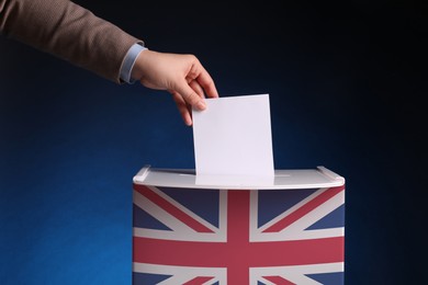 Woman putting her vote into ballot box decorated with flag of United Kingdom against dark blue background, closeup