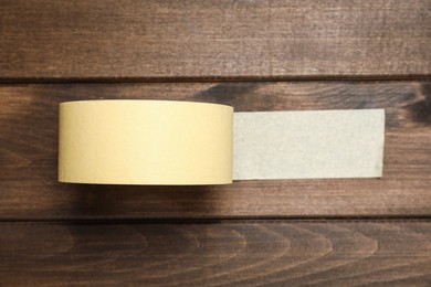 Roll of yellow adhesive tape on wooden background, top view