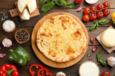 Delicious khachapuri with cheese surrounded by different products on wooden table, flat lay