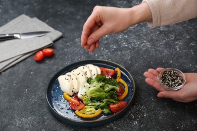 Food stylist preparing delicious salad with mozzarella and tomatoes for photoshoot at dark grey table in studio, closeup