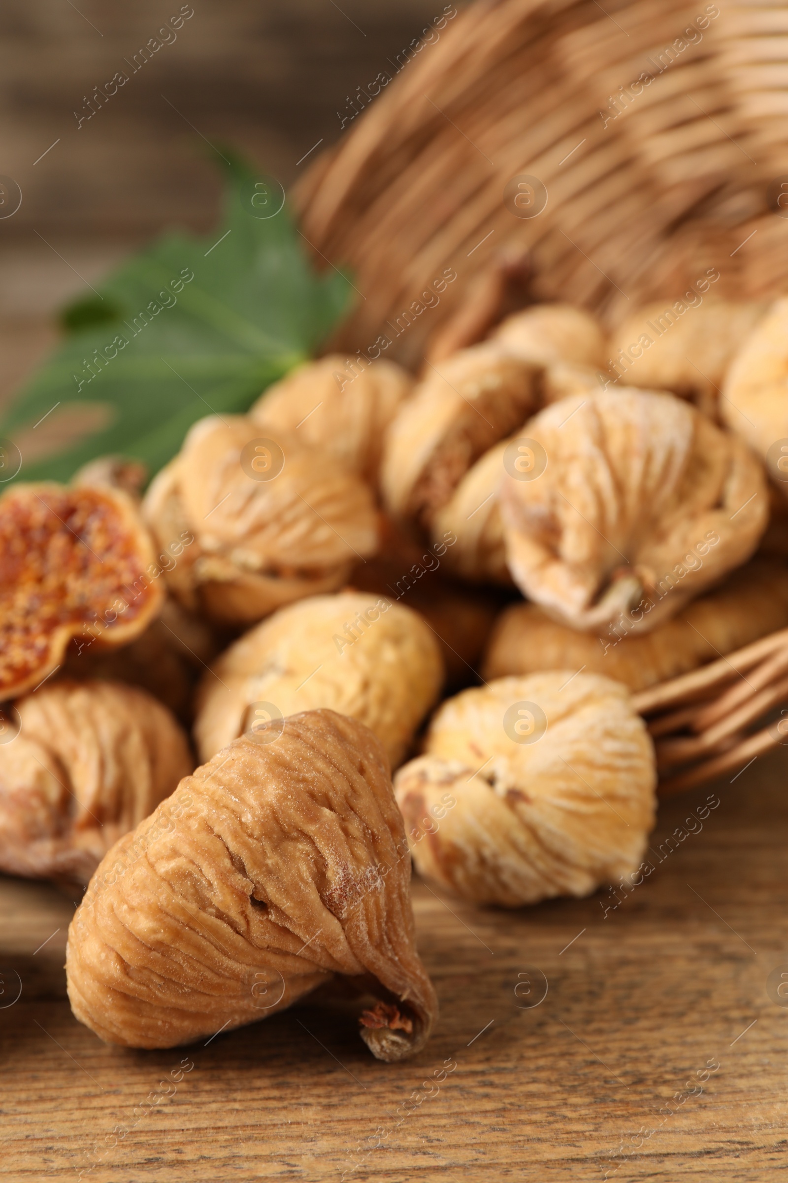 Photo of Overturned wicker basket and dried figs on wooden table, closeup