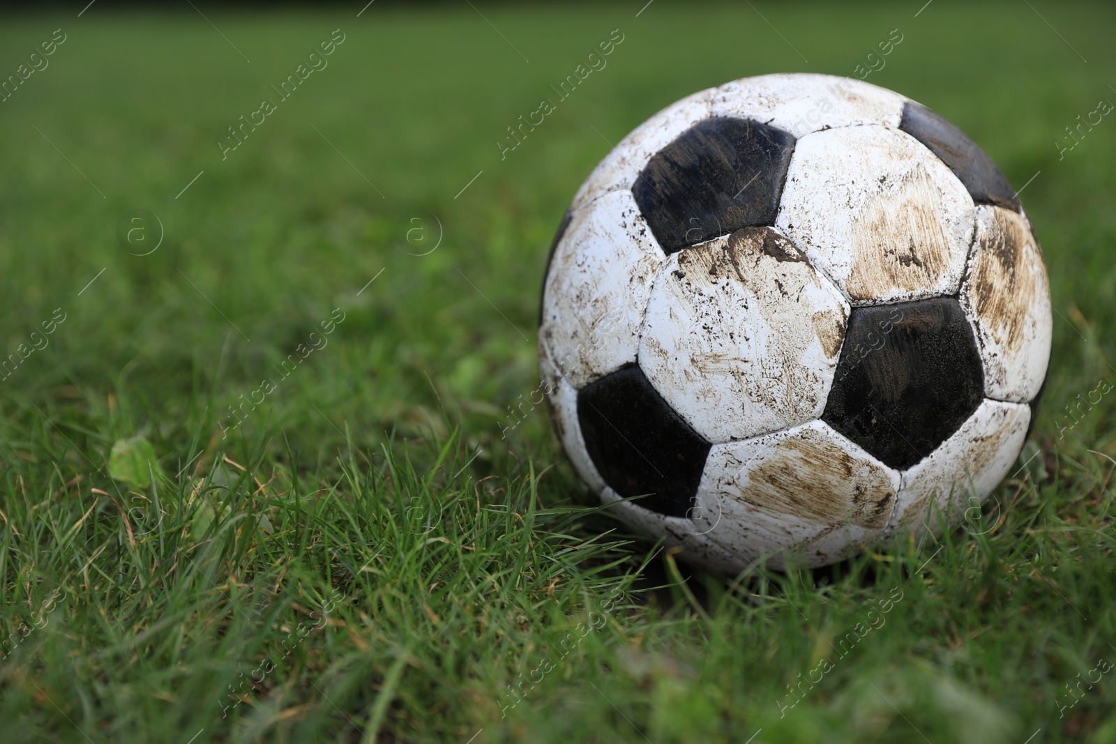 Photo of Dirty soccer ball on green grass outdoors, closeup. Space for text