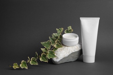 Photo of Cosmetic products, stone and ivy leaves on dark grey background