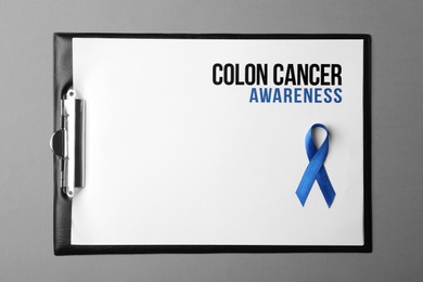 Photo of Clipboard with blue ribbon and text Colon cancer awareness on color background, top view