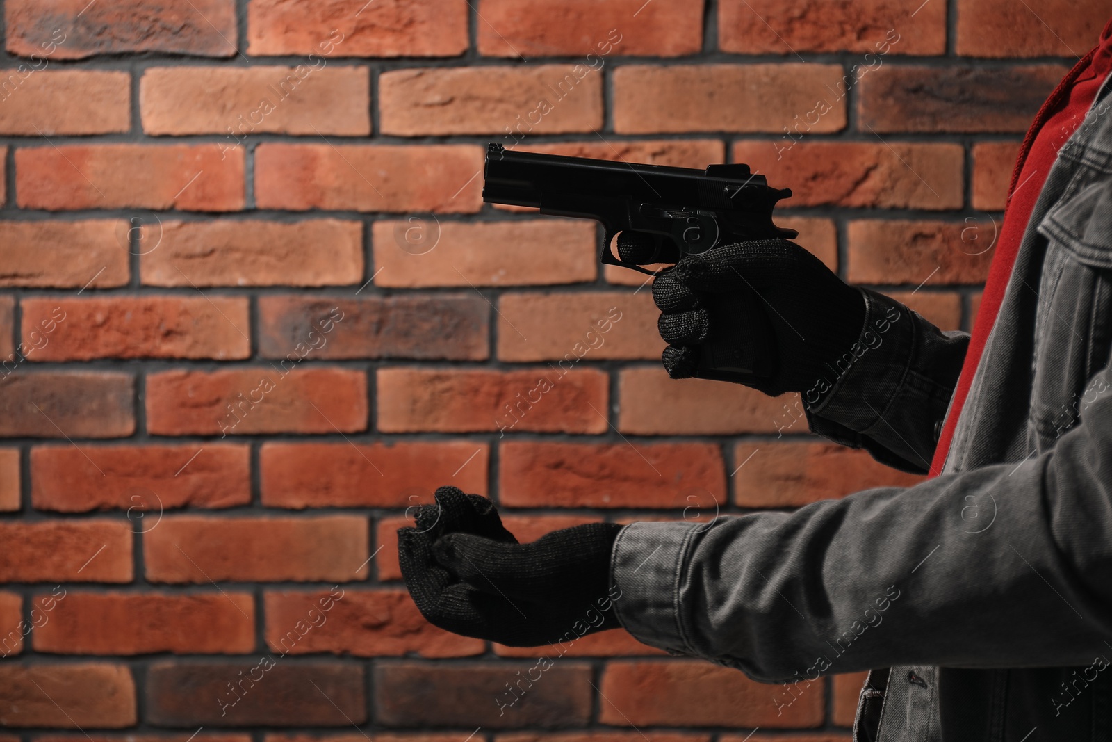Photo of Armed robbery. Dangerous criminal with gun near brick wall, closeup. Space for text