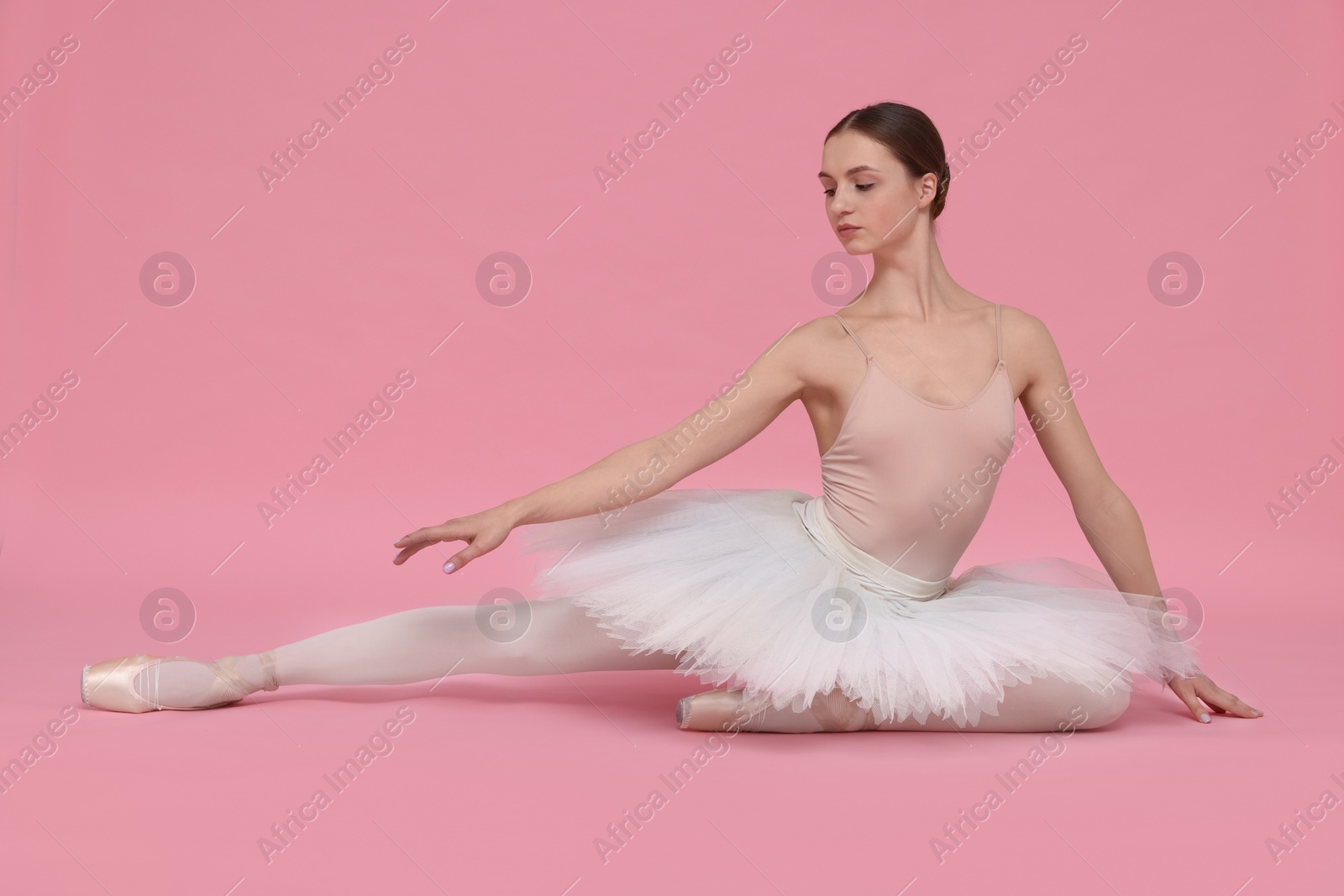 Photo of Young ballerina practicing dance moves on pink background