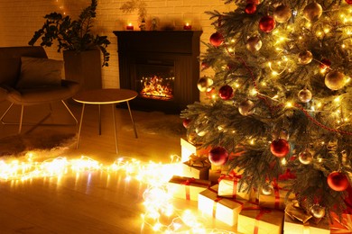 Beautiful Christmas tree with festive lights near fireplace in room