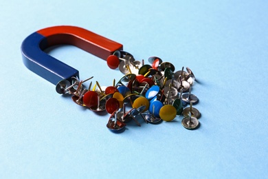 Red and blue horseshoe magnet attracting push pins on light blue background