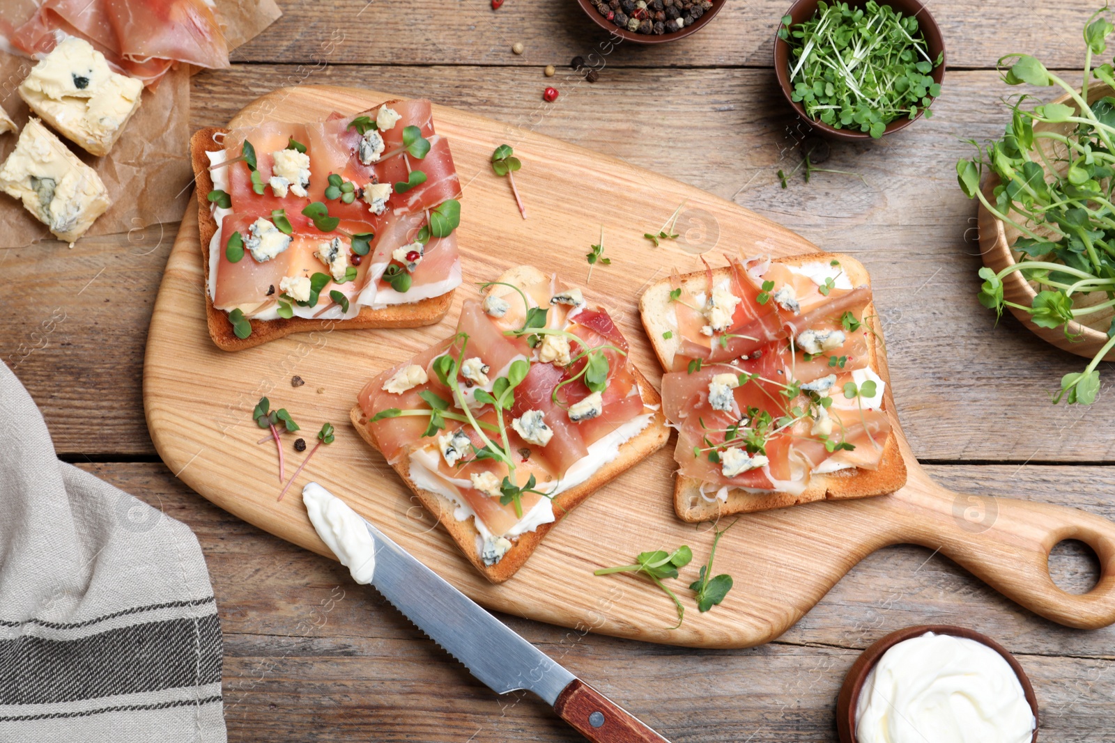 Photo of Delicious sandwiches with prosciutto, cheese and microgreens on wooden table, flat lay