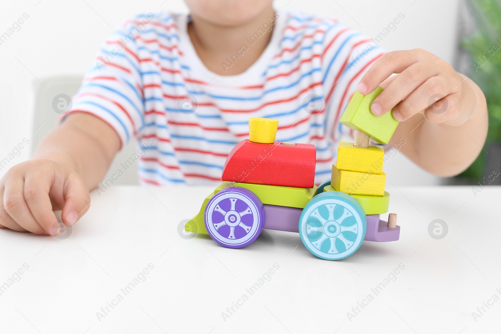 Photo of Little boy playing with toy at white table, closeup