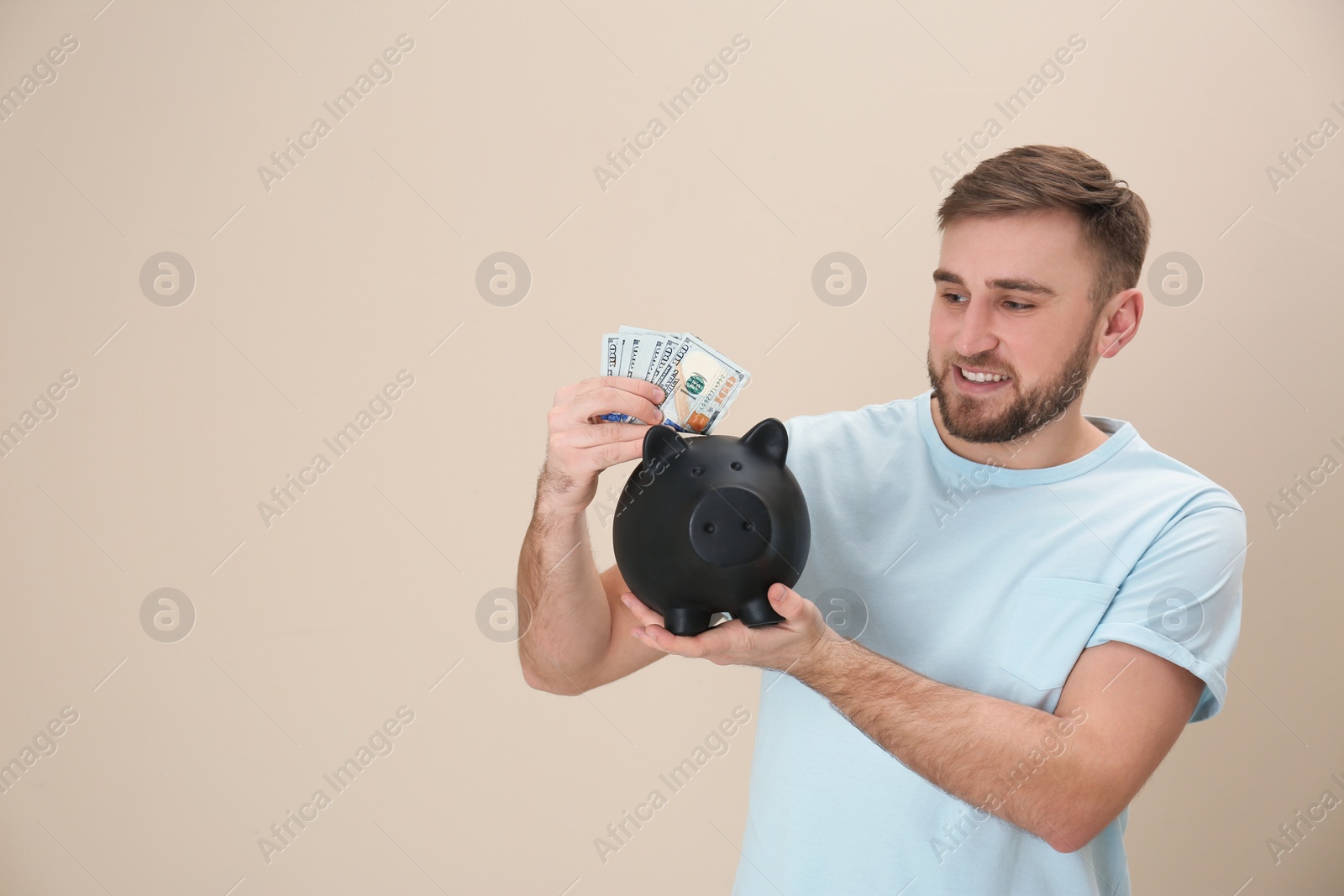 Photo of Portrait of happy young man with money and piggy bank on color background. Space for text