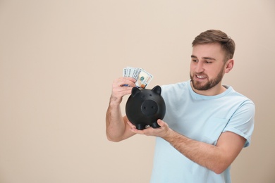 Photo of Portrait of happy young man with money and piggy bank on color background. Space for text