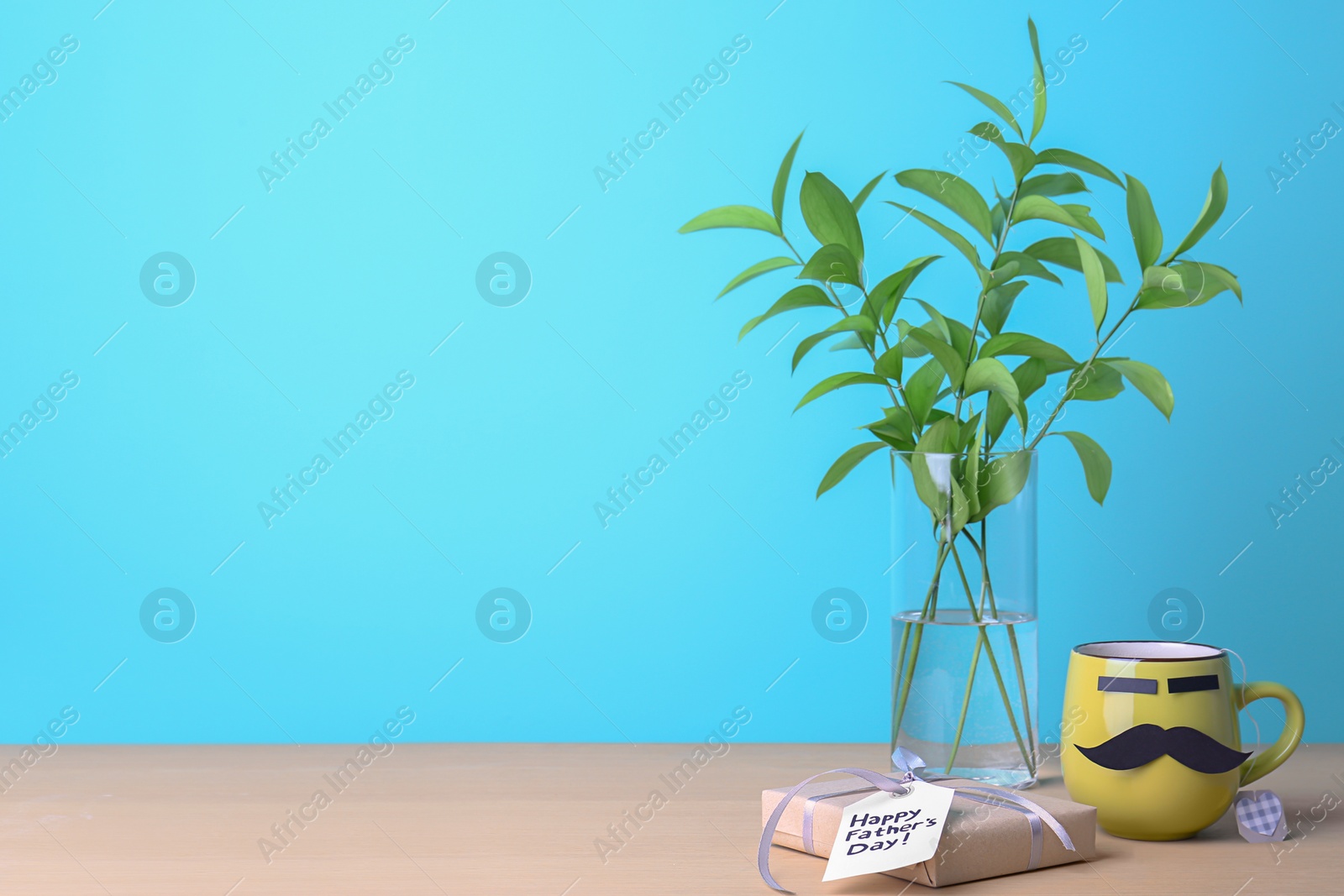 Photo of Cup with mustache and gift box on table against color background. Father's day celebration