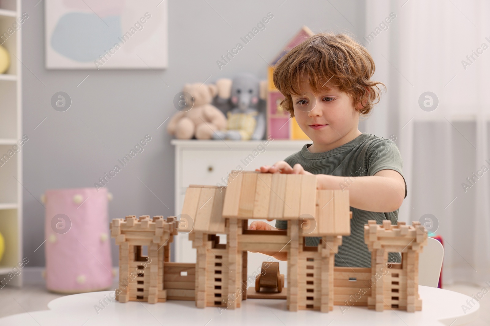 Photo of Little boy playing with wooden entry gate at white table in room, space for text. Child's toy