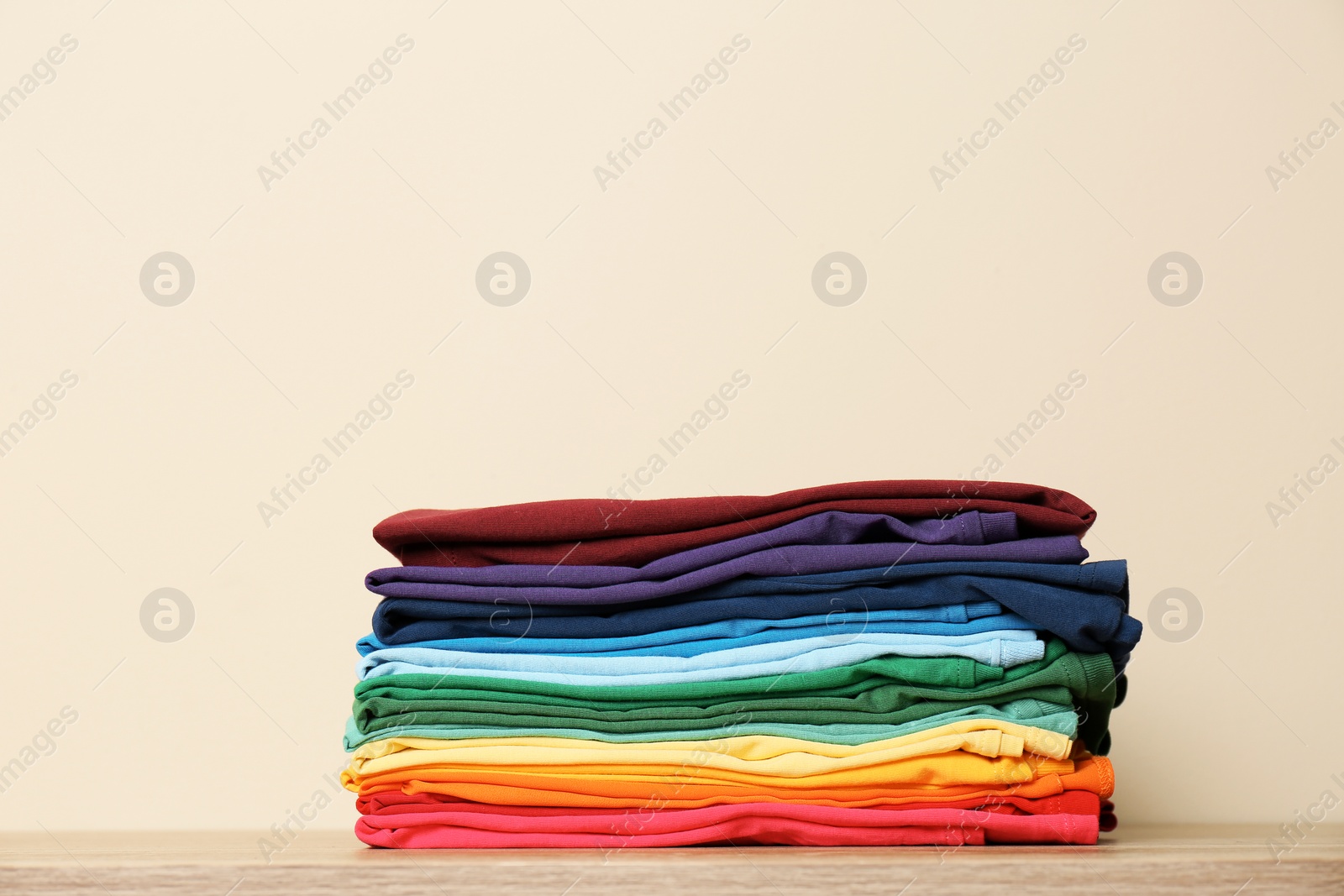 Photo of Stack of bright folded clothes on table against light background. Space for text