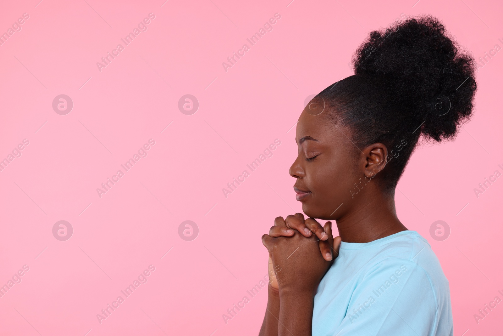 Photo of Woman with clasped hands praying to God on pink background. Space for text