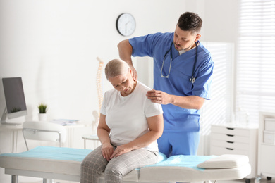 Male orthopedist examining patient with injured neck in clinic