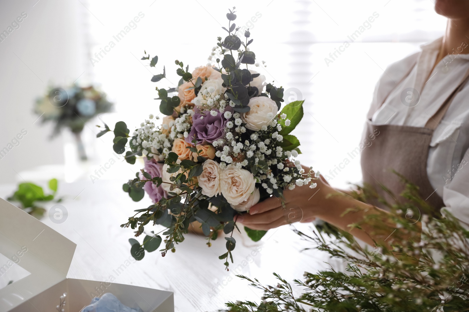 Photo of Florist holding beautiful wedding bouquet indoors, closeup