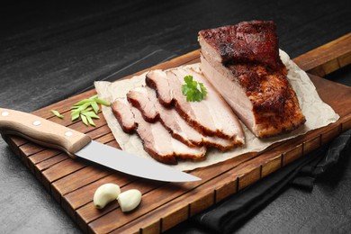 Photo of Pieces of baked pork belly served with parsley and garlic on black textured table