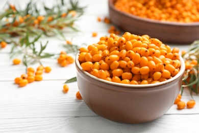 Photo of Fresh ripe sea buckthorn in bowl on white wooden table