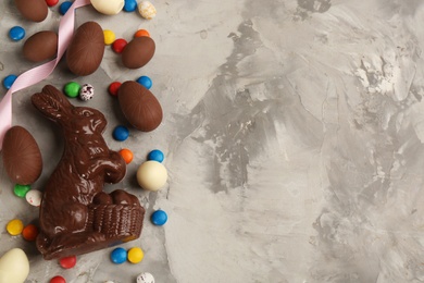 Photo of Flat lay composition with chocolate Easter bunny, eggs and candies on light grey table. Space for text