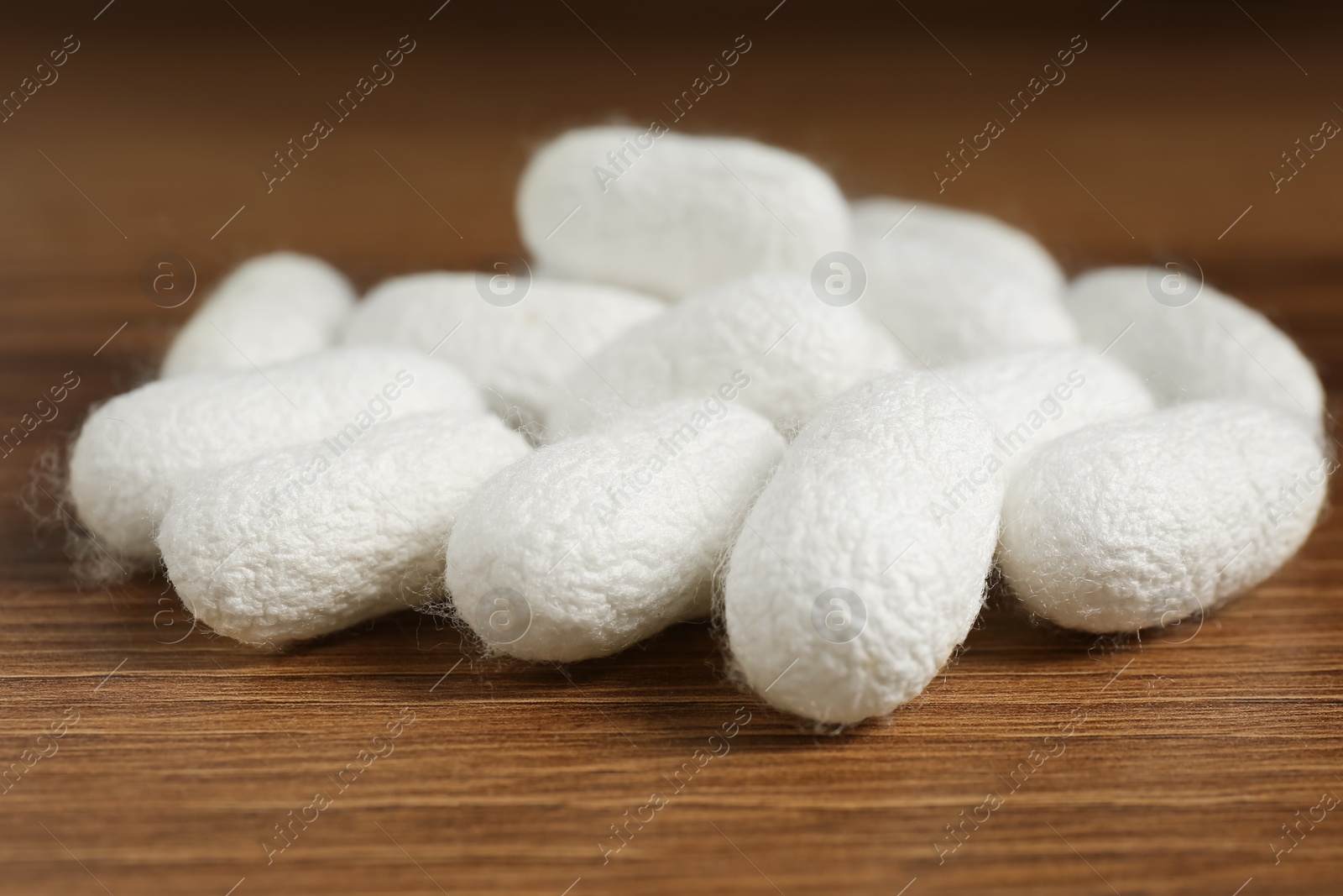 Photo of Heap of white silk cocoons on wooden table, closeup