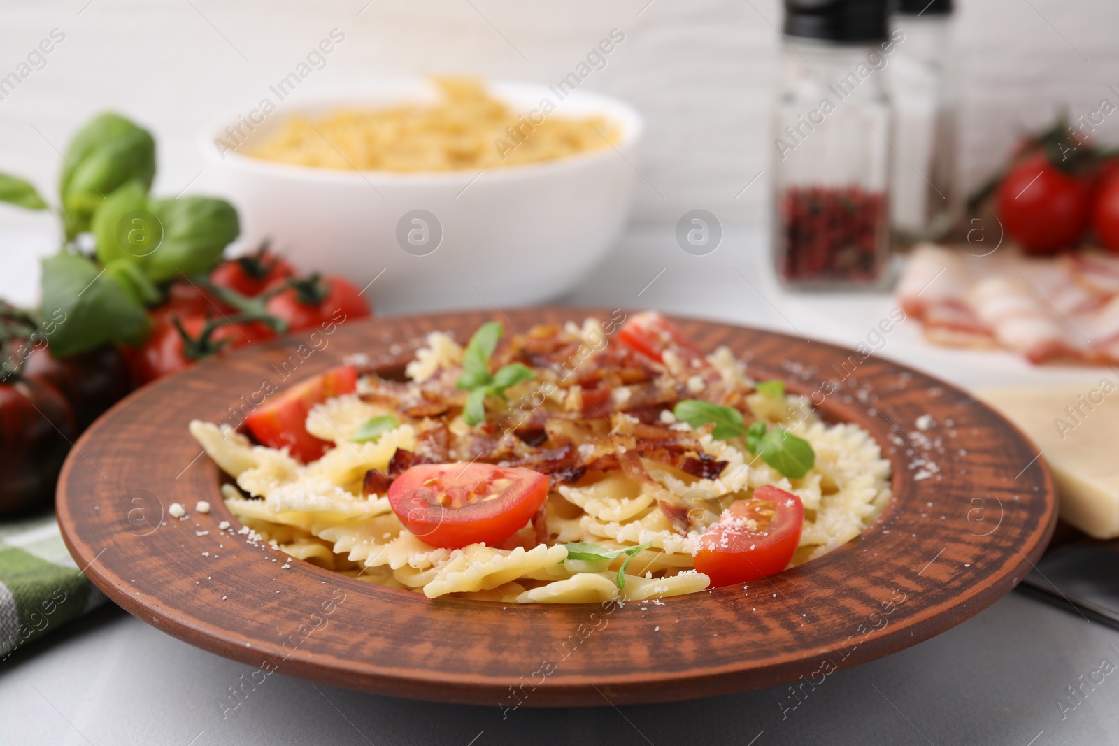 Photo of Tasty pasta with bacon, tomatoes and basil on white tiled table