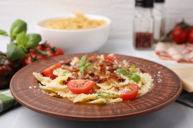 Tasty pasta with bacon, tomatoes and basil on white tiled table