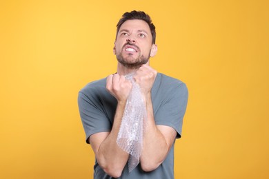 Angry man popping bubble wrap on yellow background. Stress relief