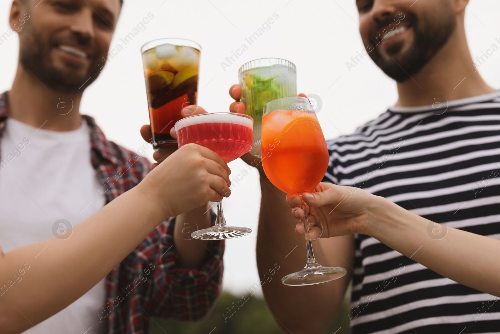 Photo of Friends clinking glasses with cocktails outdoors, closeup