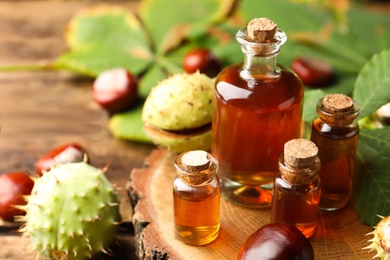 Chestnuts and bottles of essential oil on wooden table, closeup