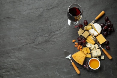 Photo of Cheese platter with specialized knives and fork and glass of red wine on grey table, flat lay. Space for text