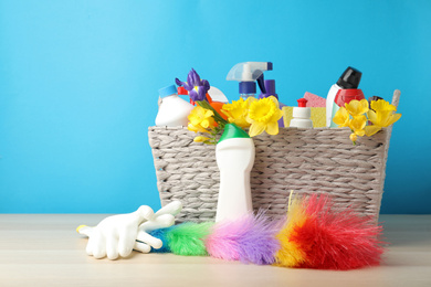 Photo of Wicker basket with spring flowers and cleaning supplies on wooden table