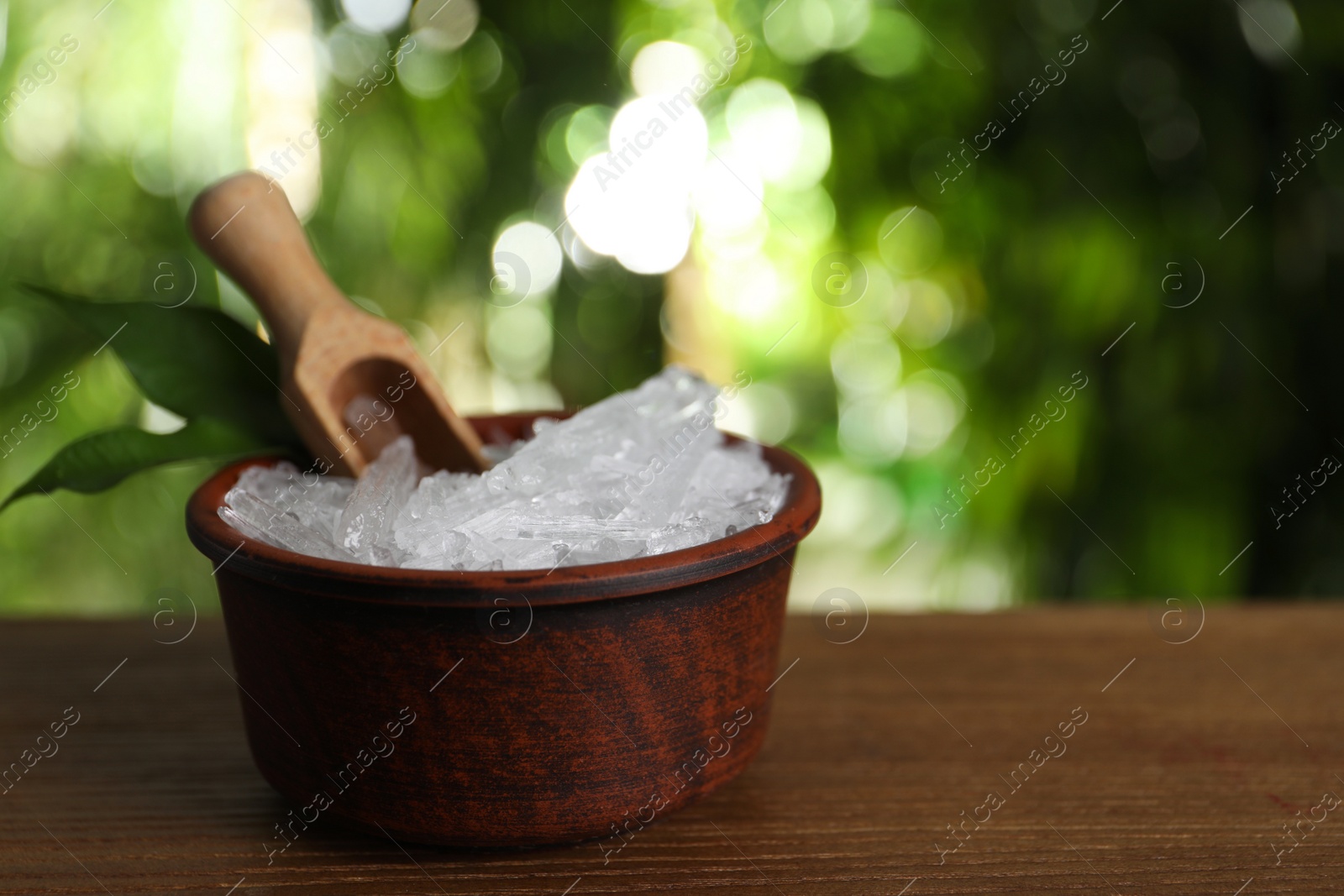 Photo of Bowl with menthol crystals, leaves and scoop on wooden table against blurred background. Space for text