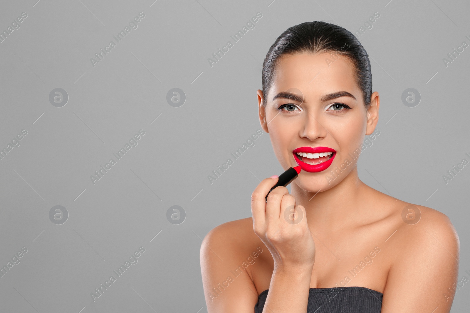 Photo of Young woman applying lipstick on color background. Space for text