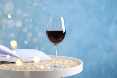 Photo of Glass of red wine and open book on white table against light blue background, space for text