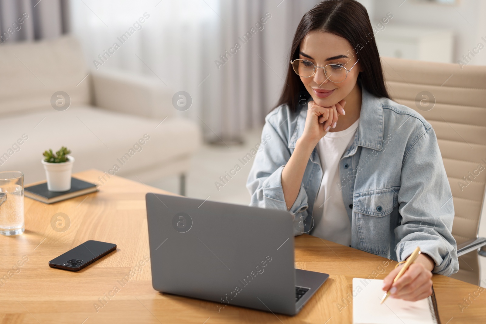 Photo of Young woman watching webinar at table in room