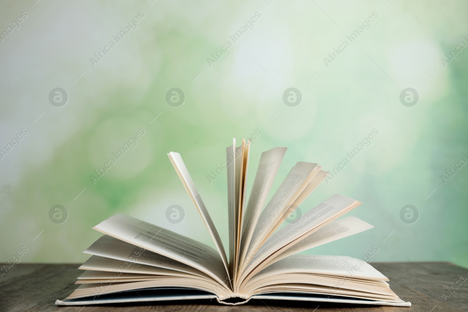 Photo of Open book on wooden table against blurred green background