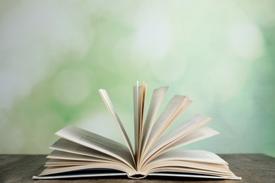 Photo of Open book on wooden table against blurred green background