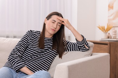 Photo of Sad woman suffering from headache on sofa indoors