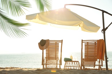 Image of Wooden sun loungers, wicker stand and outdoor umbrella on sandy beach. Summer vacation