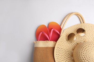 Photo of Bag with bright flip flops, sunglasses and hat on white background, flat lay with space for text. Beach accessories