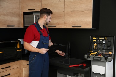 Photo of Male plumber in uniform checking faucet in kitchen. Repair service