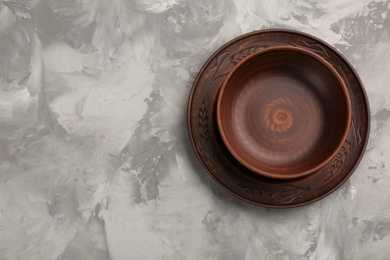 Brown clay bowl and plate on grey table, top view with space for text. handmade utensils