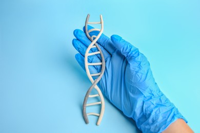 Photo of Scientist with DNA molecule model made of plasticine on light blue background, closeup