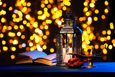 Arabic lantern, Quran, dates and Aladdin magic lamp on table against blurred lights at night