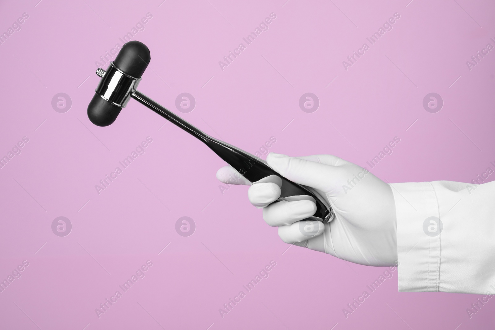 Photo of Doctor holding reflex hammer on pink background, closeup. Nervous system diagnostic