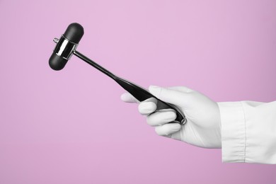 Photo of Doctor holding reflex hammer on pink background, closeup. Nervous system diagnostic
