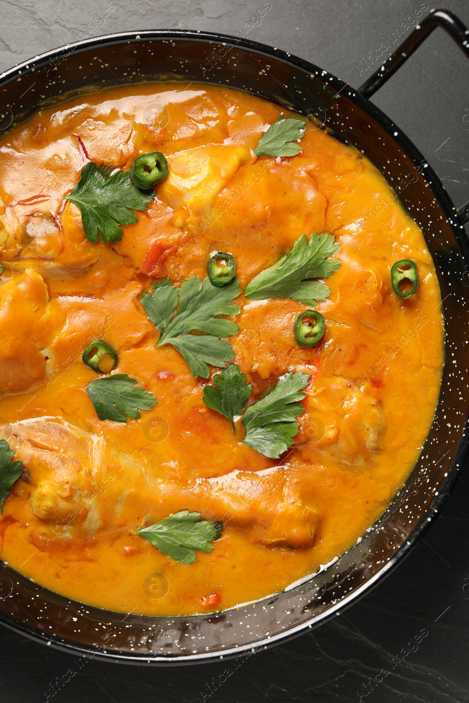 Photo of Tasty chicken curry with parsley and pepper on black textured table, top view